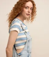 Peto corto de jeans marmorizado celeste, con tirantes ajustables, bolsillo tipo canguro y cierre lateral con botones.