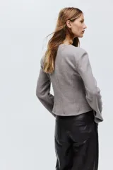 Saco entallado de punto suave, modelo corto con escote en V, hombros caídos, cierre frontal con botones y bolsillos de parche delanteros. Presenta costuras moldeadoras en la parte frontal y posterior.