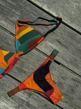 Bikini de dos piezas color marrón, con corpiño triangular fijo con corte bajo el busto, breteles regulables con hebilla y almohadillas desmontables. La bombacha es vedetina con frunce elástico en los costados.