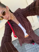 Conjunto de dos piezas compuesto por un blazer y un pantalón de corte sastrero, confeccionados en tela de algodón con estampado de rayas verticales blancas sobre fondo gris. El blazer presenta solapas clásicas y cierre frontal, mientras que el pantalón es de tiro medio y pierna recta.