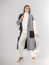 Sacón tipo tapado de corte largo, confeccionado en tejido de punto con diseño color block en tonos gris, negro y blanco. Presenta cierre frontal con botones, bolsillos laterales de parche y aberturas en los costados.