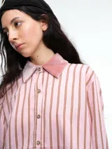 Camisa de corte relajado con estampado de rayas verticales, destacada por detalles en terciopelo en el cuello, puños y canesú. Presenta cierre frontal con botones y mangas largas.