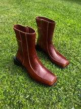 Bota corta de cuero color bordó, con punta cuadrada y taco bloque bajo. Cierre lateral con cremallera.