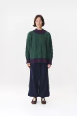 Buzo de tejido de punto con diseño de trenzas, color crema con detalles en marrón en cuello, puños y ruedo. Presenta líneas finas en contraste y pequeñas costuras decorativas en forma de cruz.