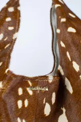 Cartera de cuero vacuno con pelo en diseño animal print similar a piel de ciervo, silueta triangular y asa integrada.