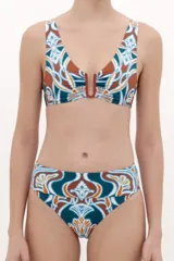 Top de bikini con escote en V profundo y detalle de herraje metálico en forma de U en el centro. Presenta un estampado geométrico multicolor en tonos terracota, azul y blanco.