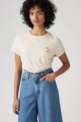 Remera color crudo de corte recto, con cuello redondo y mangas cortas con dobladillo. Tiene un bolsillo en el pecho con bordado de una flor.