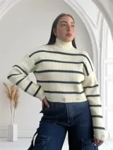 Sweater de punto grueso color crema con cuello alto y rayas horizontales negras. Tiene roturas en el ruedo.