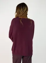 Sweater de punto con escote en V, manga larga y corte holgado. Presenta un diseño liso con costura central vertical en el frente y terminaciones acanaladas en puños y ruedo.