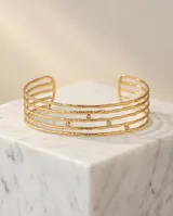 Set de cuatro brazaletes tipo esclava de acero con baño de oro, con textura martillada y detalle de circonias incrustadas.