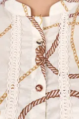 Camisa blanca con estampado de cadenas y cuerdas en tonos dorados y marrones. Tiene cuello mao, mangas cortas y detalles de encaje en el frente y la espalda.