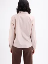 Camisa beige de manga larga con cuello camisero, cierre frontal con botones y diseño de pespuntes y bordados en relieve con formas florales en la parte inferior y lateral.