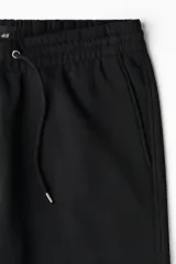 Pantalón de jogging negro de felpa pesada, corte holgado con cintura elástica ajustable mediante cordón y bolsillos laterales.