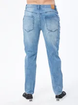 Pantalón jean de corte slim, color azul medio con efecto desgastado y sutiles roturas.