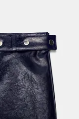 Falda mini de tiro bajo color azul marino, con efecto piel. Presenta una cintura con trabillas y un cinturón ajustable con botones a presión y tachas plateadas a contraste. Tiene forro interior a tono y cierre lateral con cremallera oculta.