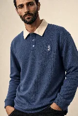 Buzo de manga larga estilo rugby color azul petróleo, con cuello beige en contraste, tapeta con botones y pequeño bordado en el pecho. Confeccionado en algodón pesado con fit relajado.