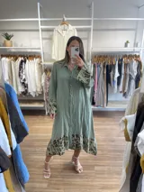 Vestido camisero largo de lino blanco con botones, cuello clásico y mangas largas con puños estampados con animal print. Tiene un corte irregular con el frente más corto que la parte trasera y estampado animal print en el ruedo.