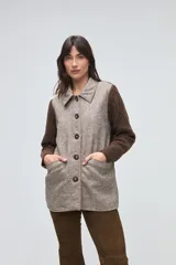 Trench de lana fina sin teñir, con diseño de textura combinada. Presenta mangas y espalda tejidas con patrón de trenzas, cuerpo liso, cuello camisero, cierre frontal con botones y bolsillos delanteros funcionales.