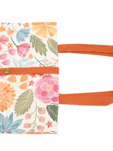 Tote bag plegable con estampado floral multicolor sobre base blanca, tiras de hombro y cinta de cierre en color tostado.