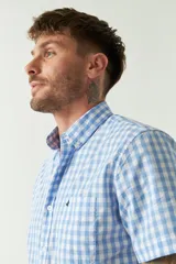 Camisa de manga corta con estampado de cuadros vichy en azul y blanco. Presenta cuello con botones, cierre frontal con botones y logo bordado en el pecho.
