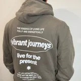 Canguro color caqui con capucha y cordón ajustable. Estampado en la espalda con la frase "The essence of living life fully and energetically", el logo "vibrant journeys", la frase "live for the present" y una cita de Santa Barbara.