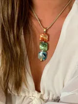 Collar con dije colgante de tres piezas cuadradas de nácar en tonos naranja, verde y azul, con engarce de bronce y cadena de cordón color beige.