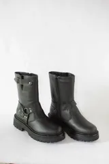 Bota de caña media confeccionada en cuero negro, con suela gruesa track antideslizante. Presenta un diseño estilo biker con estribo integrado, hebillas metálicas decorativas y una correa ajustable en la parte superior de la caña. Incluye cierre lateral para facilitar el calce.