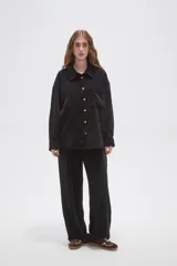 Camisa de pana negra con cuello clásico, cierre frontal de botones y bolsillo en el pecho.