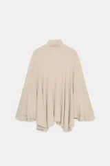 Top tipo capa de color beige, con cuello subido y cierre posterior con botones ocultos. Presenta un diseño fluido con bajo asimétrico y mangas acampanadas.