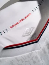 Camiseta de fútbol Umbro del Club Nacional de Football, modelo Home 2026 de manga larga. Diseño en color blanco con detalles en azul y rojo en el cuello y puños. Incluye logo de Umbro, escudo del club y sponsor Antel en el frente.