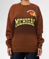 Buzo de algodón y poliéster, color azul oscuro con efecto desgastado/tie-dye. Presenta un gran estampado frontal con la palabra "MICHIGAN" en amarillo con borde negro, un corazón naranja y apliques de pines decorativos en la parte superior. Tiene cuello redondo con terminación deshilachada y bolsillo canguro frontal.