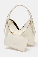 Bolso tipo mini shopper de diseño estructurado en color beige, con forma de V en la parte superior y asa de mano fija. Presenta costuras visibles y detalles metálicos en los laterales.