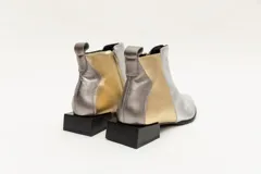 Botín corto de cuero negro con detalle de cuero dorado en el talón y textura de cocodrilo en el lateral. Tiene cierre lateral y taco cuadrado.