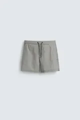 Bañador de hombre color verde claro con finas rayas blancas verticales (efecto seersucker). Tiene cintura elástica ajustable con cordón verde, bolsillos laterales y un bolsillo trasero de vivo.