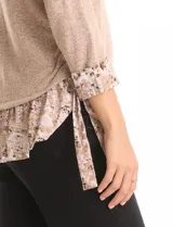 Buzo de tejido fino color beige con diseño de doble capa que simula una camisa debajo. Presenta cuello redondo, mangas largas con puños de gasa estampada en animal print, y ruedo con volado de la misma tela. Incluye detalles de frunces en los laterales.