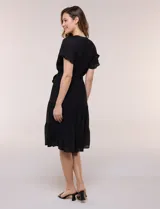 Vestido midi blanco de calce suelto y caída fluida, con escote en V, cuello a la base y apertura abotonada con detalle de puntilla. Cuenta con cintura elastizada con lazo para anudar a tono, mangas cortas con volados y falda con volantes escalonados.