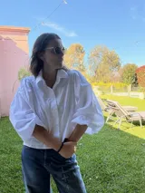 Camisa de color marrón oscuro con cuello clásico y mangas abullonadas con puños elásticos. Presenta un corte holgado y cierre frontal con botones.