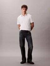 Chomba de piqué blanca Calvin Klein, de corte regular y manga corta, con cuello clásico con líneas grises en contraste y cartera de dos botones. Cuenta con el monograma CK bordado discretamente en el pecho.