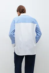 Camisa celeste con rayas verticales blancas, de corte amplio y cuello camisero clásico. Presenta bolsillo de parche en el pecho, espalda lisa en color blanco y puños abotonados.