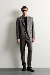 Blazer gris de corte regular fit con patrón a cuadros, confeccionada en tejido con mezcla de lana. Cuenta con cuello de solapa de muesca, cierre frontal de botonadura sencilla, bolsillos con solapa en la cadera, bolsillo de vivo en el pecho y aberturas en la espalda.