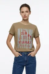 Remera de manga corta color beige, con cuello redondo y diseño al cuerpo. Presenta un estampado frontal multicolor de estilo veraniego con temática marina y detalles con glitter.