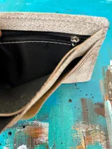 Billetera compacta blanca con diseño artístico pintado a mano en tonos turquesa, marrón y negro, perteneciente a la línea Ottenta.