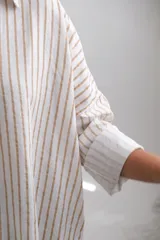Blusa de corte holgado con estampado de rayas verticales en tonos beige y blanco. Presenta cuello camisero con escote en V, mangas largas con puños anchos y dobladillo redondeado.