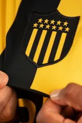 Camiseta de fútbol Puma del Club Atlético Peñarol, modelo Away Jersey Dandelion, color amarillo con finas líneas horizontales negras y detalles en negro en cuello y mangas. Incluye el logo de Puma, el escudo del club y el sponsor Antel en el frente.