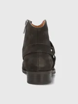 Bota corta de gamuza color marrón oscuro, con diseño de correa decorativa con tachas metálicas y hebilla lateral. Cuenta con cierre lateral para un ajuste cómodo y suela de goma.