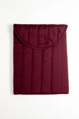 Funda acolchada para laptop color bordó, con diseño capitoneado de líneas verticales y solapa curva con cierre.