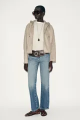 Chaqueta bomber de efecto ante en color marrón, con capucha ajustable mediante cordones, cierre frontal con cremallera, bolsillos laterales y bajo con elástico interior.