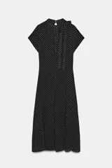 Vestido midi de viscosa con estampado de lunares blancos sobre fondo negro. Presenta cuello redondo con detalle de lazada, manga corta y pliegues en la cintura con bajo recto.