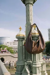Cartera tipo bolso de hombro con diseño saca, confeccionada en cuero con textura de cocodrilo en color marrón oscuro y detalle de nudo en el asa.