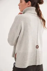 Polera de calce relajado con cuello alto, confeccionada en lana. Presenta un diseño bicolor con cuerpo en gris claro y mangas con estampado jacquard de arabescos en tonos tierra y negro. Incluye detalle de costura central vertical en el frente.